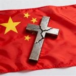 Broken Christian cross laying atop a Chinese flag
