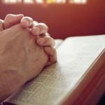 Hands praying over a bible